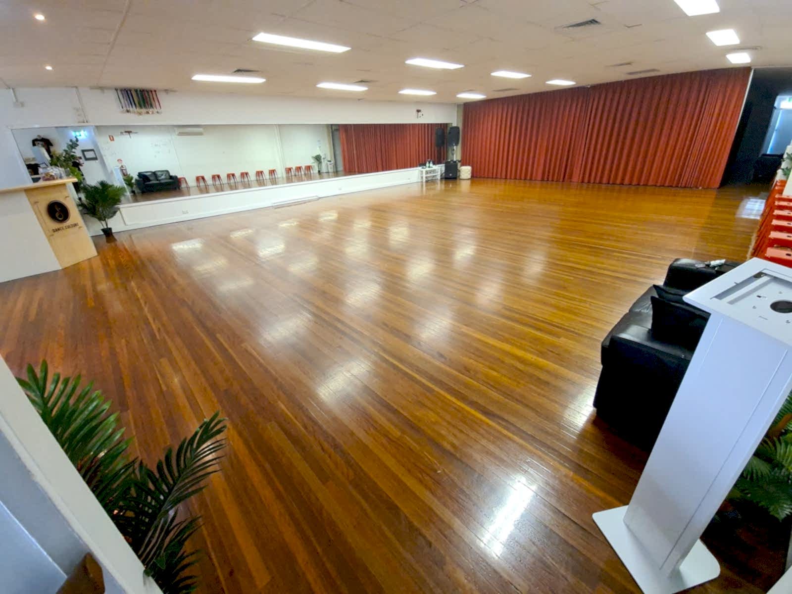 Studio 1 at Dance Culture Annerley: a large polished hardwood dance floor with full-length mirrors and red stage curtains