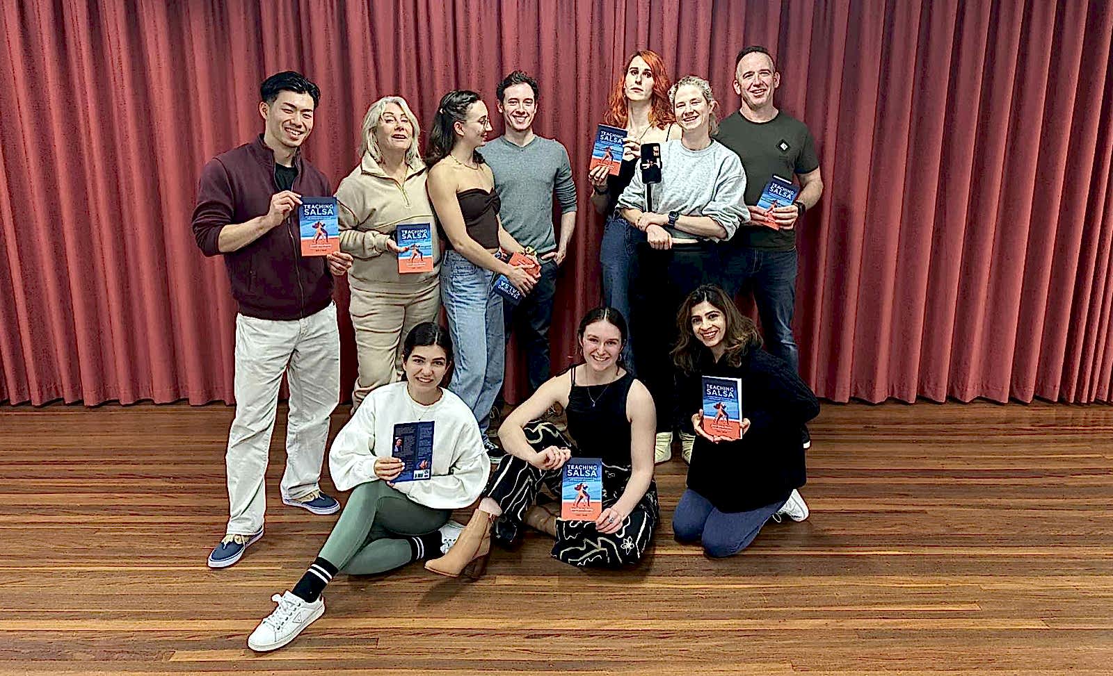 A Dance Culture instructor training cohort holding their copies of Teaching Salsa