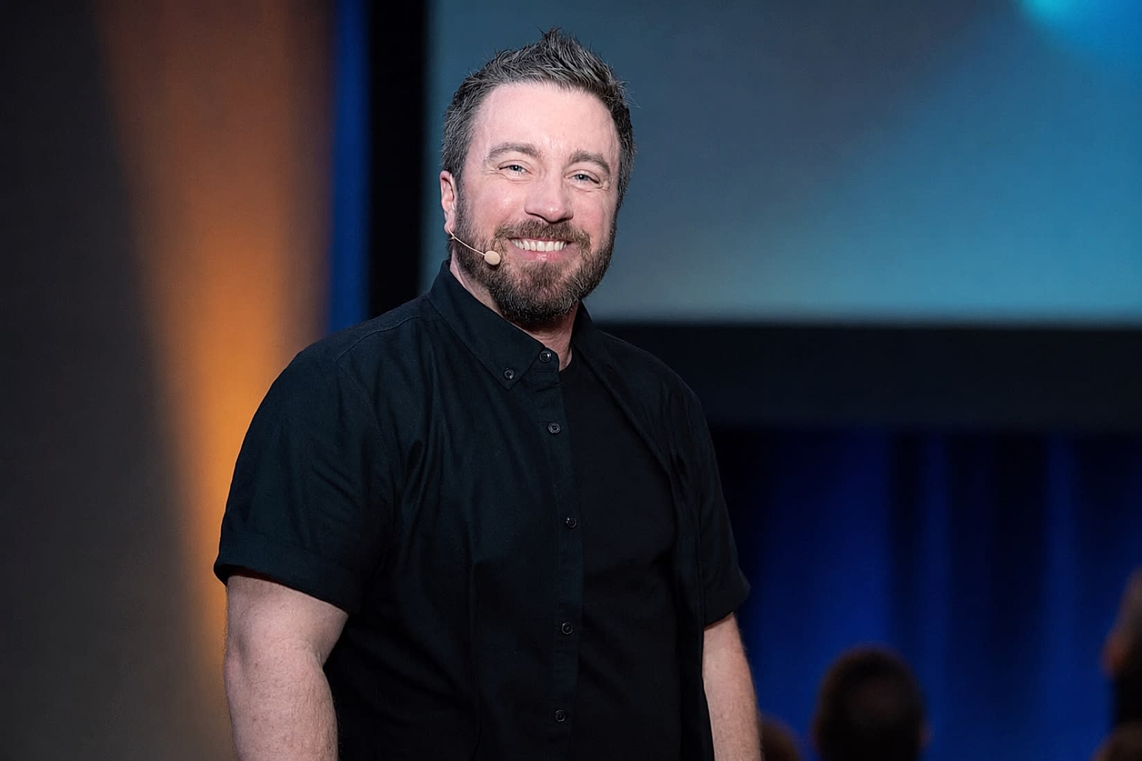 James Quinn-Hawtin speaking on stage with a headset microphone